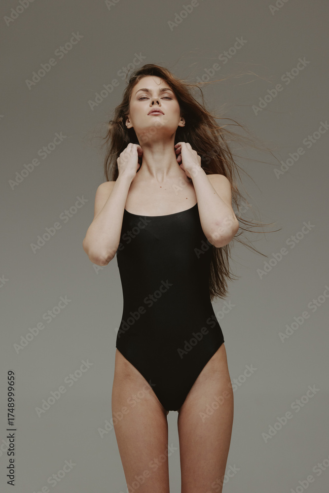 Fototapeta premium Woman in black swimsuit posing confidently with flowing hair and neutral background, showcasing elegance and strength.