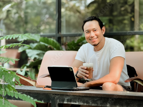 Happy smile man drink iced cocoa while working online with his tablet computer in the cafe.
