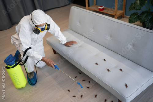 Pest control Exterminator in workwear and respirator mask spraying pesticide in sprayer bottle on cockroaches inside house.