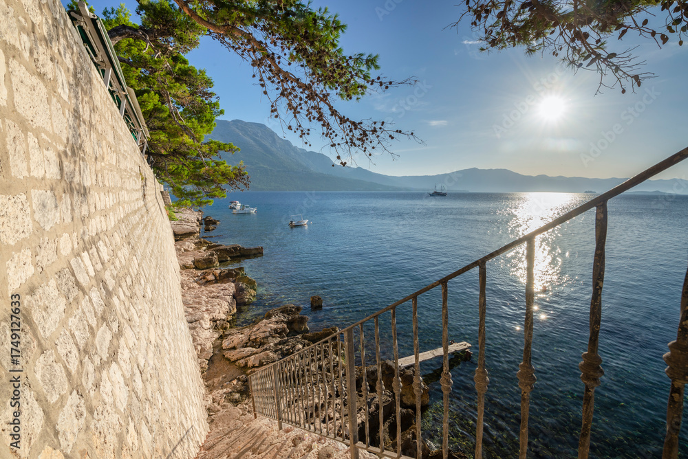 Obraz premium Treppe hinunter zu Felsen am Wasser unterhalb der Stadtmauer von Korcula mit Blick auf Kanal und Berge von Peljesac, Dalmatien, Kroatien