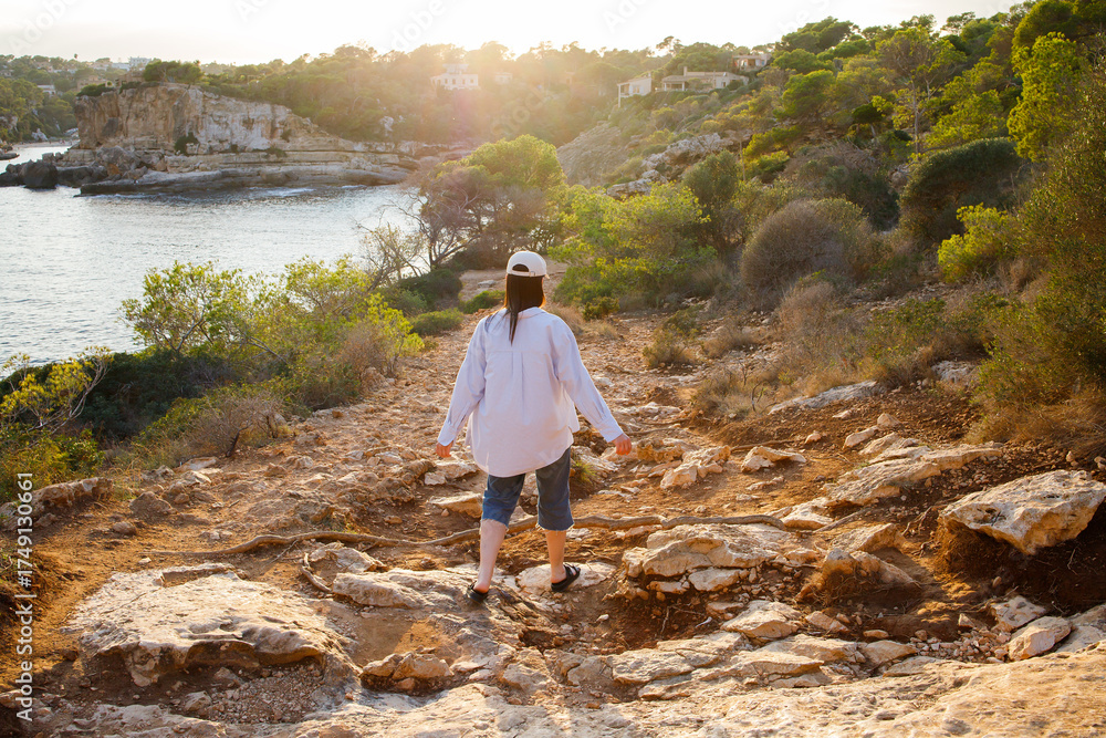 Naklejka premium Brunette girl in white cap hiking near the sea on sunset