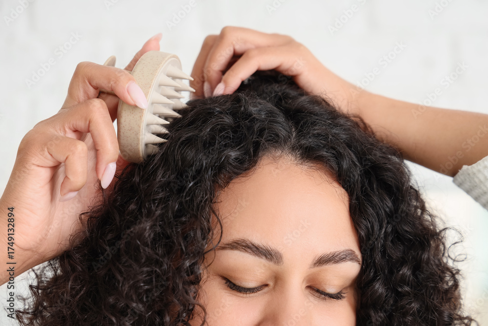 Naklejka premium Beautiful young African-American woman using scalp massager for her healthy curly hair at home