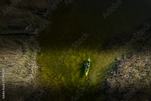 Fototapeta Naklejka Na Ścianę i Meble -  Top-down drone shot of kayaker near wooden dock and boat on clear green lake with reeds in Mazury, Poland, summer outdoor adventure