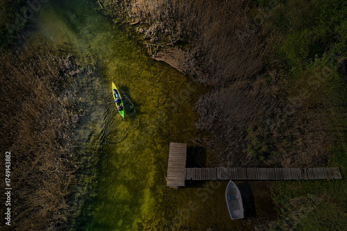 Fototapeta Naklejka Na Ścianę i Meble -  Top-down aerial of river meandering through dense forest with lone kayaker in Mazury, Poland during summer, tranquil nature scene