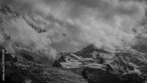 High resolution image of a dramatic helicopter mountain rescue from the French Alps of the Mont Blanc mountain range with cloudy dramatic skies and a distant Helicopter with a stretcher hanging below
