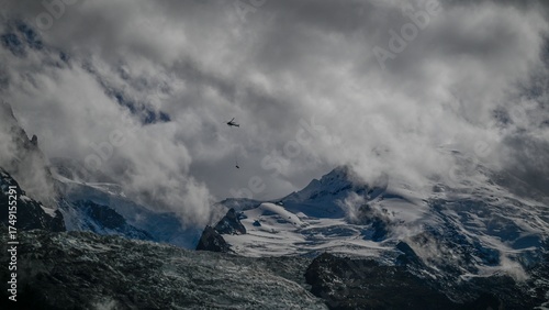 High resolution image of a dramatic helicopter mountain rescue from the French Alps of the Mont Blanc mountain range with cloudy dramatic skies and a distant Helicopter with a stretcher hanging below