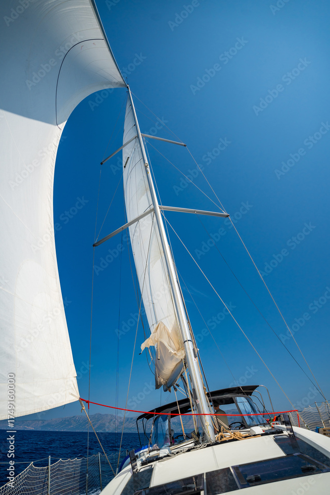 Fototapeta premium White sails filled with wind, seen from the bow of a sailing yacht near Croatia. Freedom, clean energy, adventure and mindful travel on the open sea.