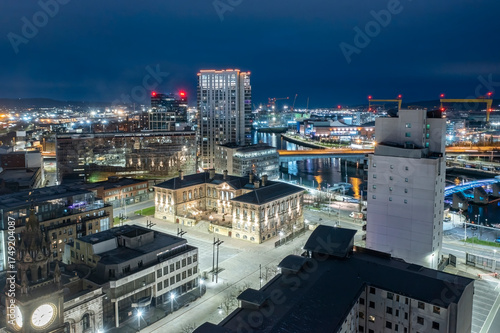 Night aerial view of Belfast cityscape with the illuminated Custom House and nearby buildings by the waterfront.