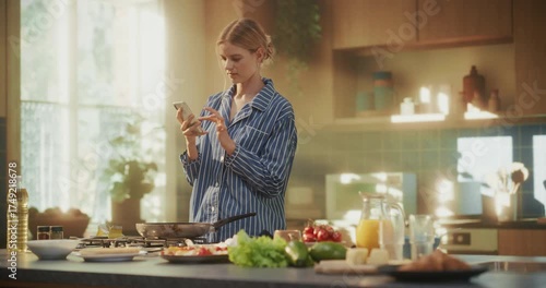 Wallpaper Mural Female Preparing Morning Meal in a Bright Kitchen. Wearing Pajamas, She Holds a Spatula in One Hand and Scrolls Through Her Smartphone with the Other, Looking for New Breakfast Ideas Online Torontodigital.ca