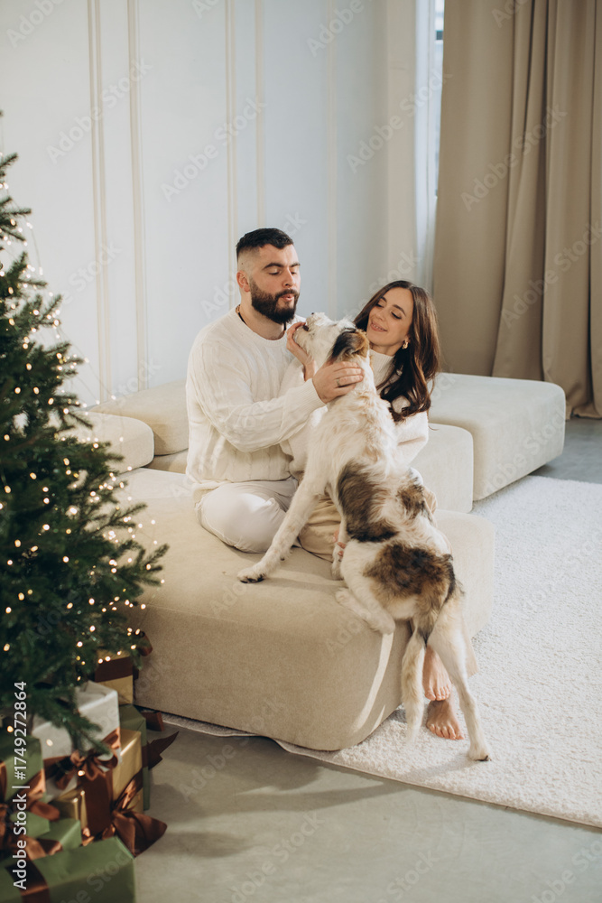 Obraz premium Couple petting dog near christmas tree with gifts