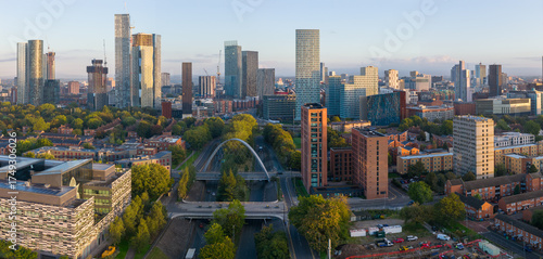 Aerial sunrise view above Princess Road featuring Manchester’s skyline framed by trees and modern architecture.