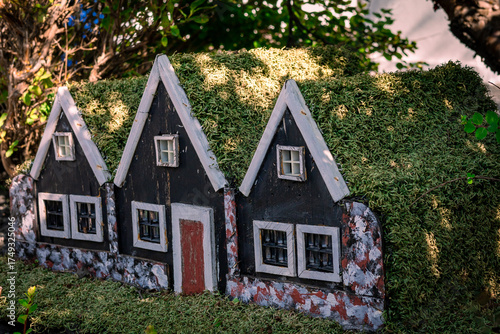 Garden decoration three small black wooden elf houses with green moss roof, typical for Iceland. 