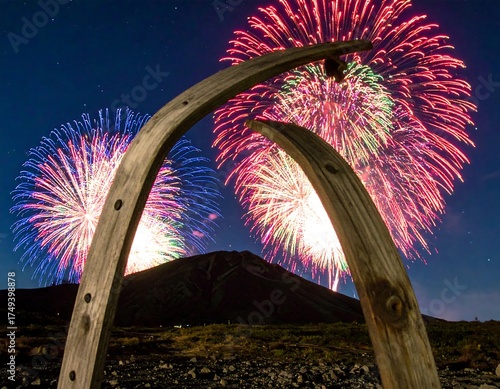 A night scene captures vibrant fireworks bursting behind a dark mountain peak framed by a wooden archway under a starlit sky