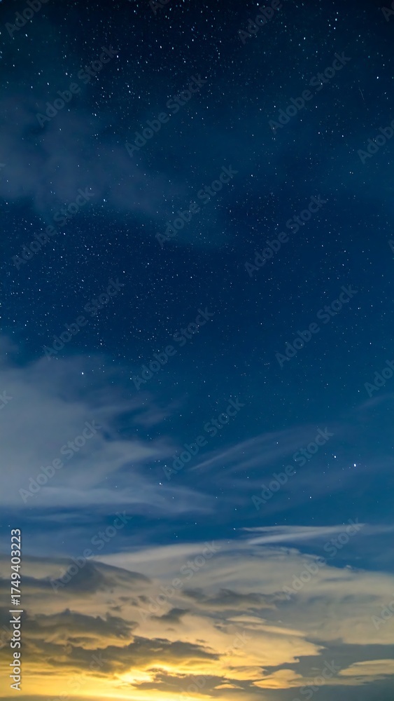 Fototapeta premium A night sky photograph featuring a gradient from a golden horizon, through clouds, to a deep blue with shimmering stars