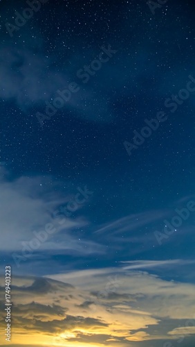 A night sky photograph featuring a gradient from a golden horizon, through clouds, to a deep blue with shimmering stars