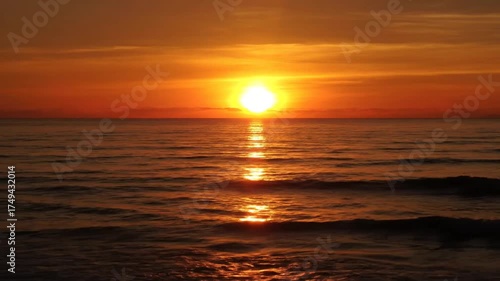 Orange sunset over ocean horizon with warm sunlight reflecting on water