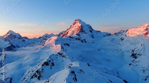 Snow capped mountain peaks at sunrise with blue sky and golden light