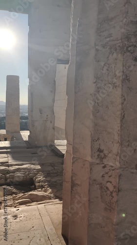 View through an ancient marble doorway among the columns of the Acropolis in Athens, Greece. Warm sunlight highlights the textures of the stone architecture and opens up to a panoramic view 