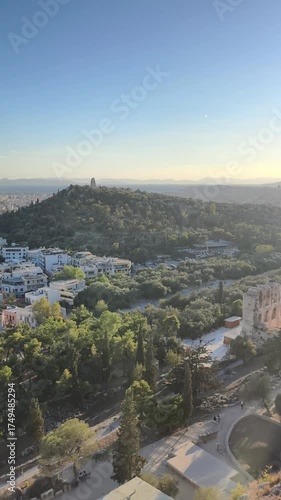 View of the ancient Odeon of Herodes Atticus seen from the Acropolis in Athens during golden hour. The sun sets over the olive-covered hills, casting warm light on one of Greece’s most iconic 