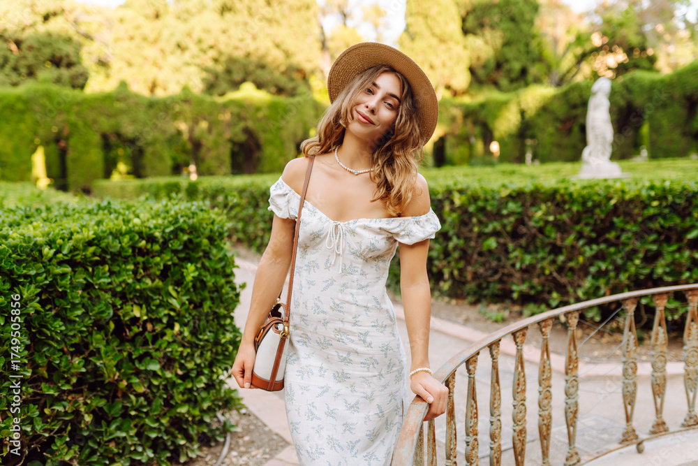 Obraz premium Young woman in a summer dress enjoying the sunshine in a beautiful garden setting during the late afternoon