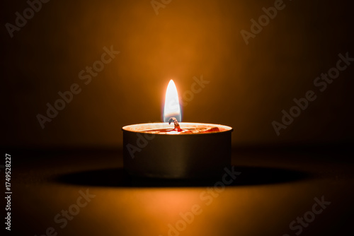 Small burning candle in small container on dark black background. Closeup. Front view.