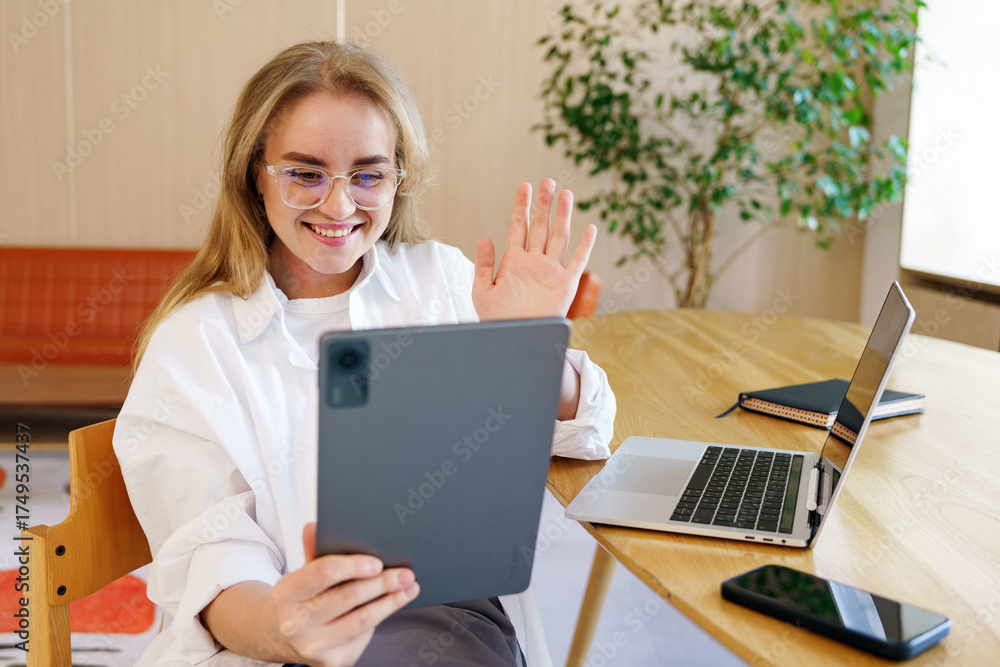 Fototapeta premium Person smiling and waving while video calling in a cozy workspace
