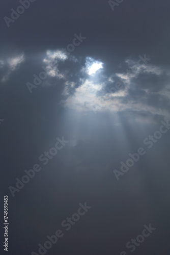Sun rays break through thunderclouds. Dark sky background. Vertical photograph