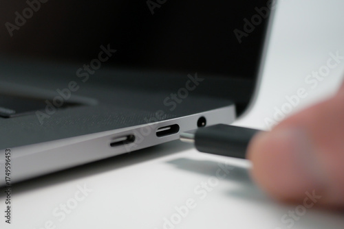 Hand plugging in a USB Type C cable into a port on a modern notebook or laptop computer. Close up.