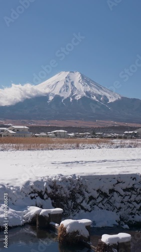 山梨県忍野村より除く雪に覆われた田園風景越しの富士山のタイムラプス映像（縦・パンニング）