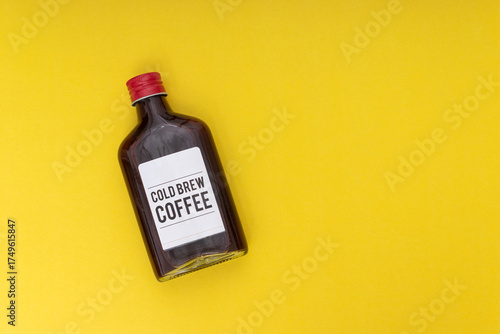cold brew coffee bottle on yellow background, minimalist composition