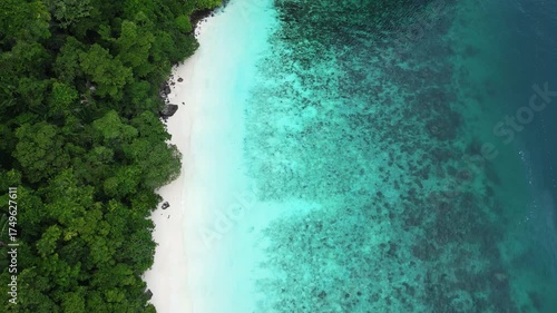 Aerial view of Monkey Beach on Ko Phi Phi Island, Thailand, showing turquoise sea, white sandy beach, tropical jungle and traditional long tail boats anchored near the shore.