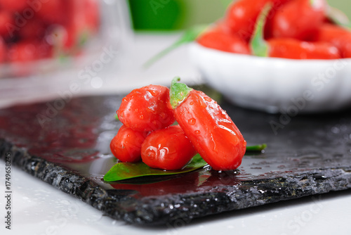 Bild auf Leinwand Fresh Red Goji Berries Wolfberries from Ningxia on Slate Board with Green Leaves