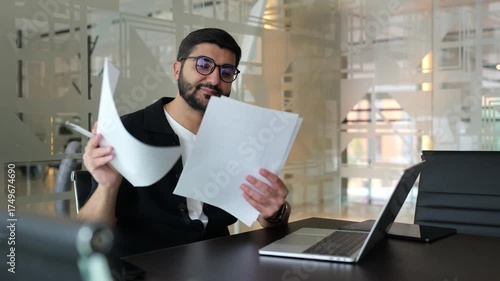 Young man reviewing documents while sitting at a desk in a modern office, showcasing focus and determination during work hours