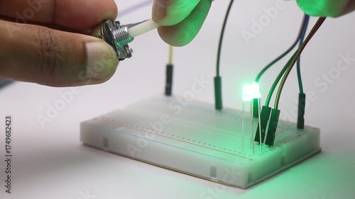 Small LED with jumper cable connected on a breadboard and is being controlled by a potentiometer. Dimming of light with variable resistance