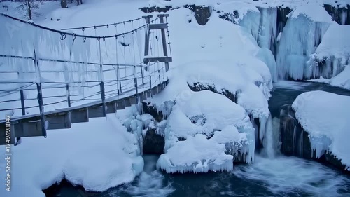 Suspension bridge and frozen waterfall in a snowy winter landscape.