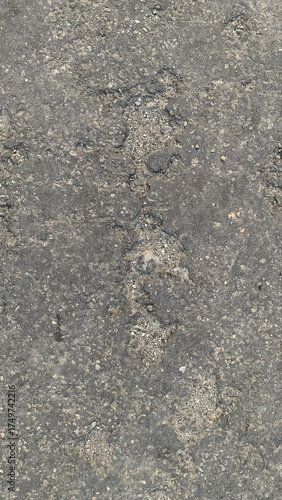 Detailed full-frame background texture of rough, damaged, dark gray asphalt pavement featuring embedded small gravel and vertical lines of erosion and cracking. Construction concept