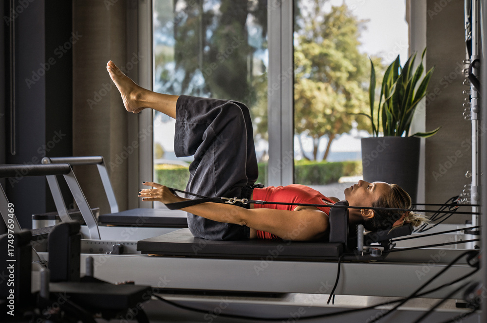 Obraz premium Woman doing pilates exercise on reformer in gym with sea view