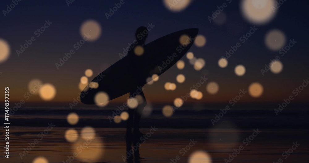 Naklejka premium Walking wetsuit-clad surfer holding surfboard on wet sand at dusk, with bokeh orbs reflecting sky