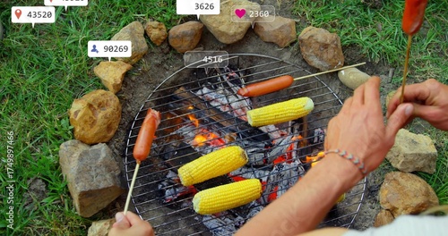 Friends roasting corn and hot dog skewers over backyard fire pit, with grill grate, glowing coals