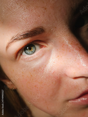 Close-up of oily skin with cream, freckles, and a blue eye under natural light. texture, detail.