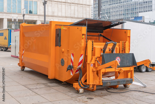 Tableau sur toile A large orange industrial waste compactor stands on a city square
