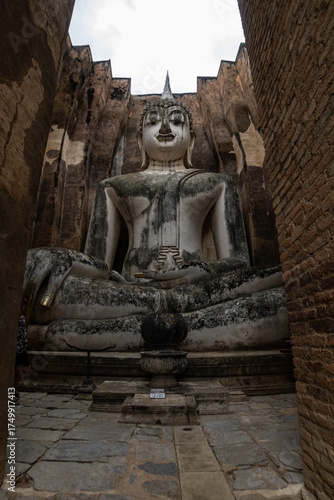 Monumental Buddha image Phra Atchana in subduing mara posture at Wat Sri Chum temple Sukhothai Historical Park, ancient stuccoed brick sculpture, thailand cultural heritage landmark