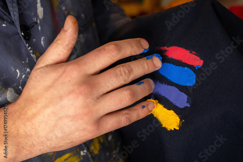 Artisan's hand testing ink colors (red, blue, yellow) on dark fabric. Close-up detail of screen printing for textile printing in a craft workshop.