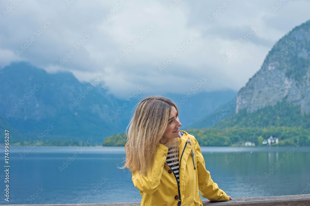 Fototapeta premium Woman in Yellow Jacket Admiring Hallstatt Lake, Austria. Travel and Tourism Concept in Scenic Alpine Village