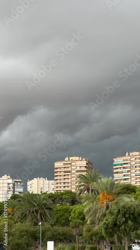 Alicante, Spain — October 9, 2025: Ominous storm clouds loom over palm‑lined beachfront apartment buildings along the Costa Blanca as rain threatens