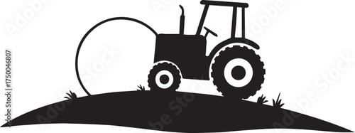 Black tractor with hay bale on grassy hill silhouette