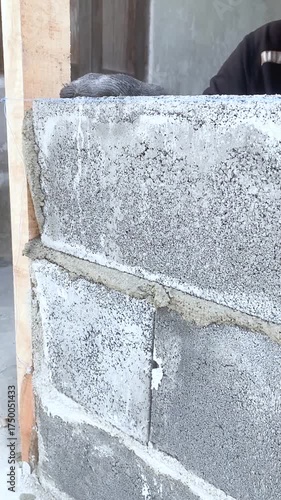 Construction worker laying concrete blocks with cement mortar at building site. Close-up of hands during masonry work under sunlight, showing texture and building process.