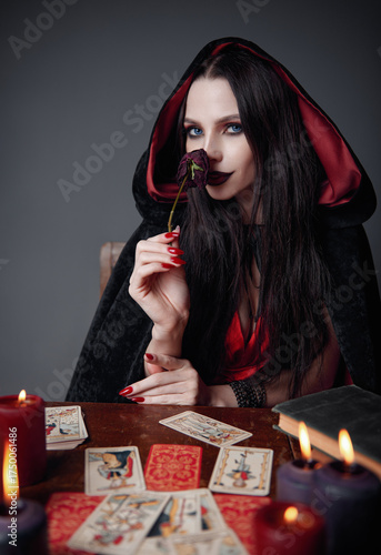 Dark beauty: gorgeous young sorceress sniffs a withered rose. Portrait of smiling witch. Pretty diviner in black robe