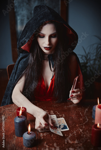 Dark beauty: lovely young soothsayer reading tarot cards. Gorgeous sorceress making Taro layout. Beautiful witch in black cloak