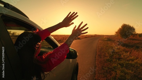 Young female passenger catches wind with hands from car window. Beautiful girl student in car drives road to meet sunrise. Family trip, teenage girl traveling by auto. Family vacation. People travel